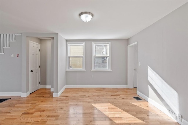 empty room featuring stairway, light wood-style floors, visible vents, and baseboards