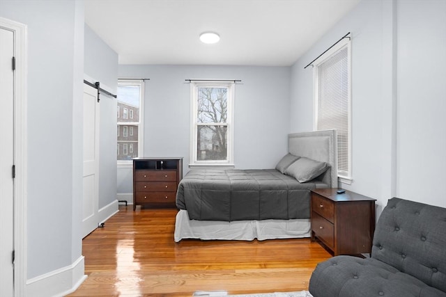 bedroom with a barn door, wood finished floors, and baseboards