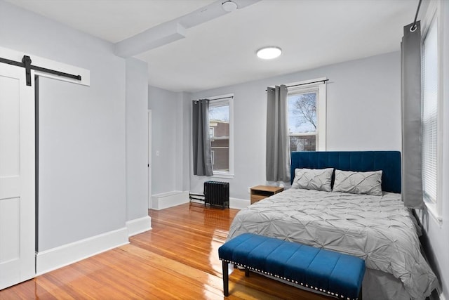 bedroom featuring radiator, a barn door, light wood-style flooring, and baseboards