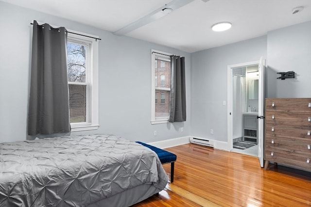 bedroom with a baseboard heating unit, wood finished floors, and baseboards
