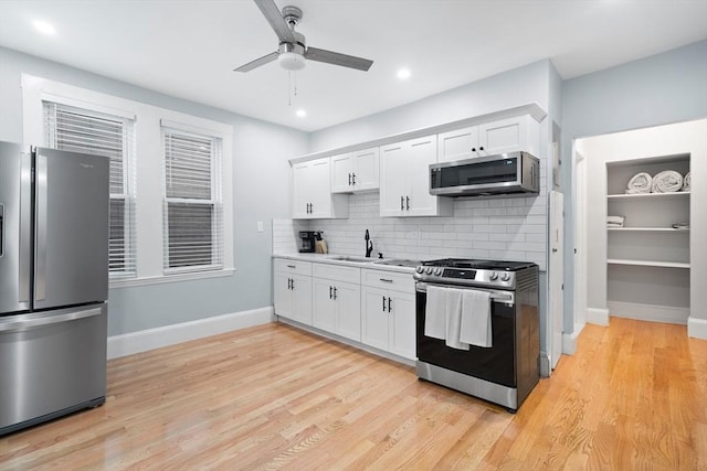 kitchen featuring appliances with stainless steel finishes, a sink, ceiling fan, white cabinetry, and tasteful backsplash