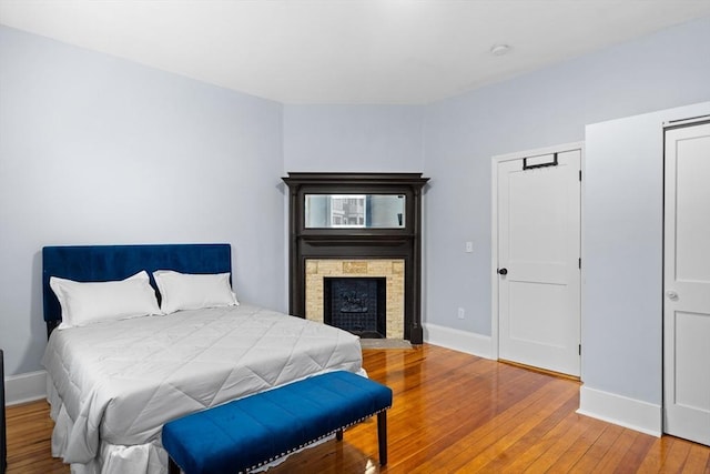 bedroom with hardwood / wood-style flooring, baseboards, and a fireplace with flush hearth