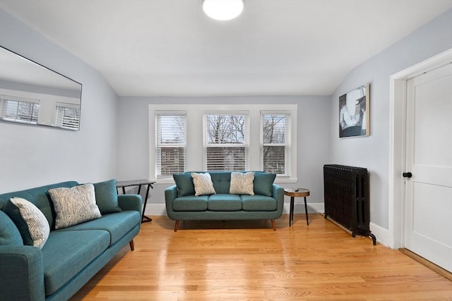 living area with radiator heating unit, vaulted ceiling, light wood-type flooring, and baseboards