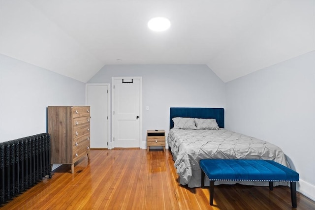 bedroom featuring lofted ceiling, light wood-type flooring, and radiator