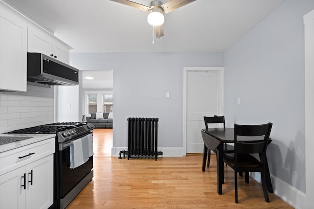 kitchen featuring stainless steel gas range, exhaust hood, white cabinets, and radiator heating unit