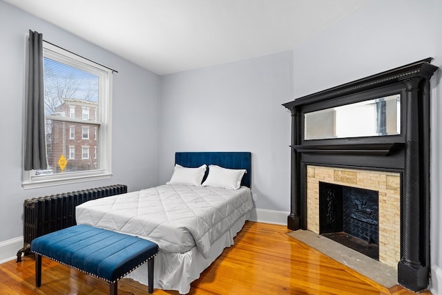 bedroom with a stone fireplace, hardwood / wood-style flooring, and radiator