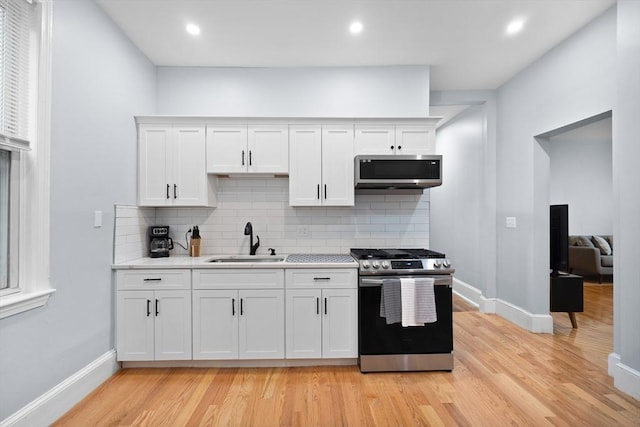 kitchen featuring appliances with stainless steel finishes, a sink, light countertops, light wood-style flooring, and white cabinetry