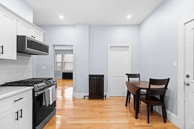 kitchen with light hardwood / wood-style floors, stainless steel appliances, radiator heating unit, and white cabinetry