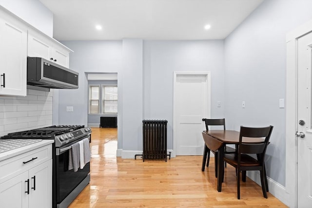 kitchen featuring radiator heating unit, stainless steel appliances, decorative backsplash, white cabinets, and light countertops