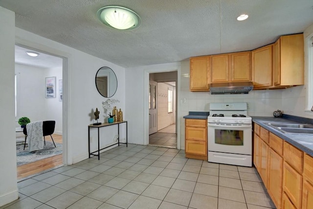 kitchen featuring light tile patterned floors, white range with gas stovetop, a sink, and dark countertops