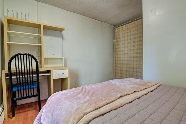 bedroom with a textured ceiling, baseboard heating, and wood finished floors