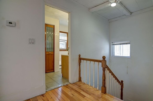hallway featuring an upstairs landing, light wood finished floors, and beamed ceiling
