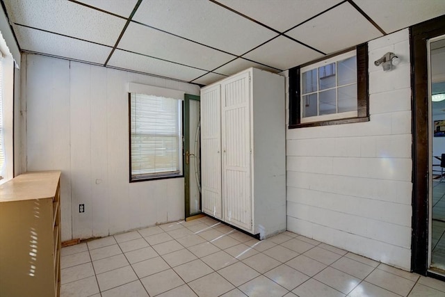 unfurnished bedroom featuring wood walls, light tile patterned floors, and a paneled ceiling
