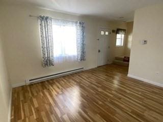 empty room featuring baseboards, wood finished floors, and a baseboard radiator