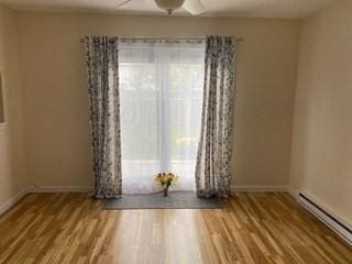 unfurnished room with wood finished floors, baseboards, ceiling fan, and a baseboard heating unit