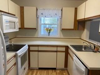 kitchen featuring white appliances, light countertops, white cabinets, a sink, and light wood-style flooring