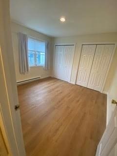 unfurnished bedroom featuring two closets, recessed lighting, a baseboard heating unit, and wood finished floors