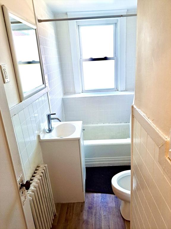 full bathroom with vanity, plenty of natural light, radiator, and tile walls