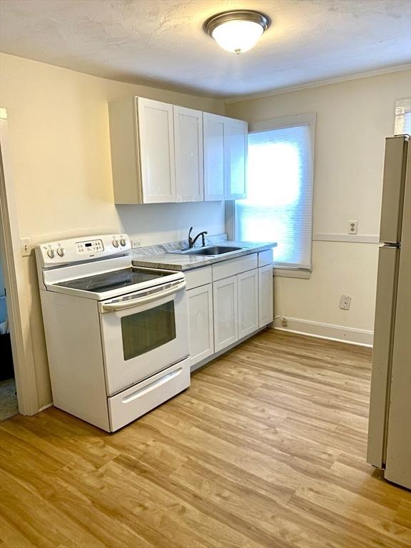 kitchen with white cabinetry, refrigerator, sink, and electric range