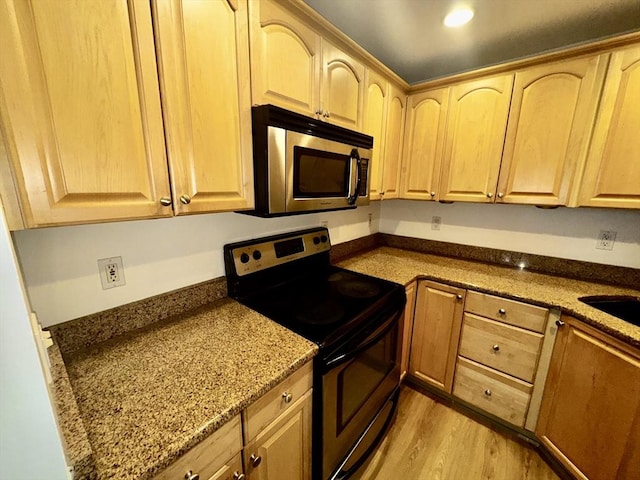 kitchen with stainless steel appliances, light brown cabinetry, stone counters, and light wood-type flooring