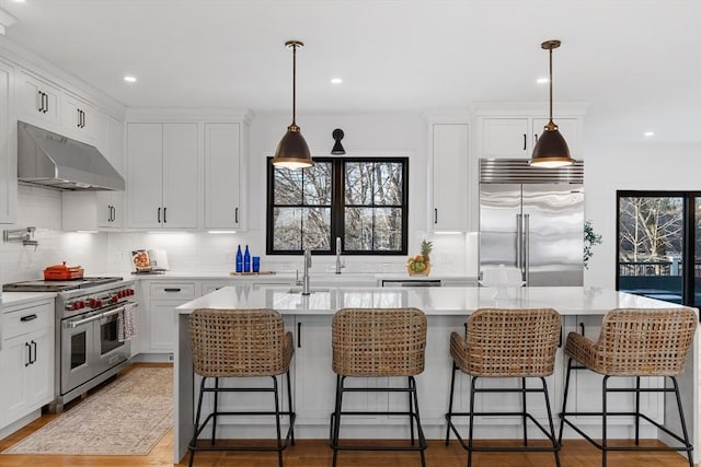 kitchen featuring an island with sink, high end appliances, and white cabinets