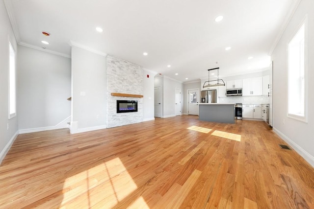 unfurnished living room featuring ornamental molding, visible vents, light wood-style floors, and a fireplace