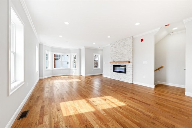 unfurnished living room featuring light wood finished floors, baseboards, visible vents, crown molding, and a stone fireplace