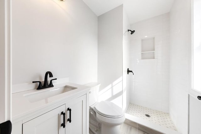 bathroom with a tile shower, vanity, and toilet