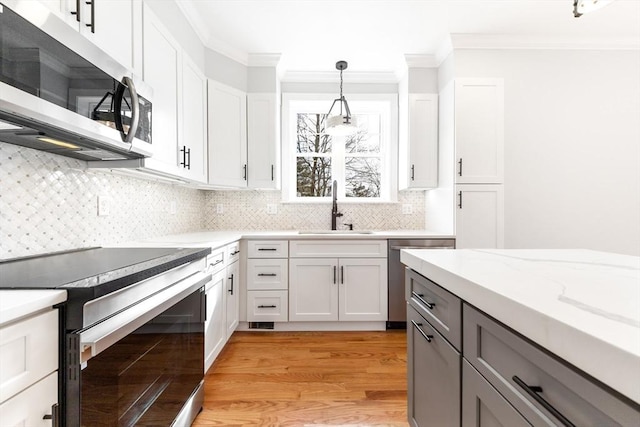 kitchen featuring stainless steel appliances, ornamental molding, hanging light fixtures, and a sink