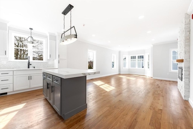 kitchen with a center island, decorative backsplash, ornamental molding, a sink, and a stone fireplace