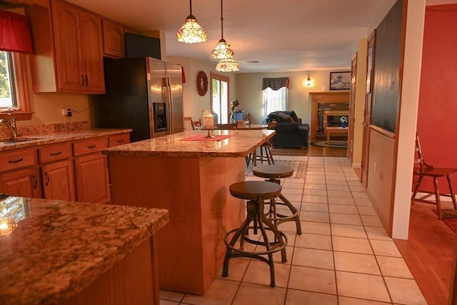 kitchen featuring stainless steel fridge, a fireplace, a wealth of natural light, a kitchen bar, and a kitchen island