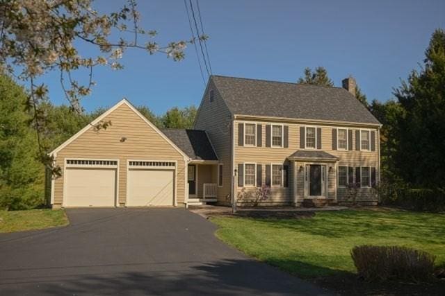 colonial home with a garage, a front yard, driveway, and a chimney