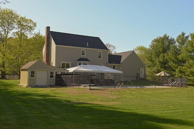 rear view of property with an outdoor structure, fence, a chimney, a gazebo, and a lawn