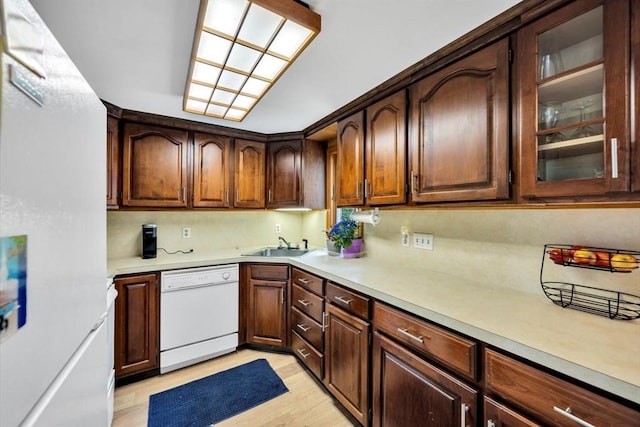 kitchen featuring white appliances, light countertops, light wood-type flooring, and a sink