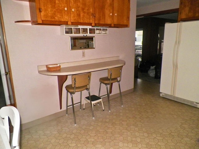 7 Maple Ln, Millbury, MA 01527 - kitchen featuring freestanding refrigerator, a breakfast bar, light countertops, brown cabinetry, and baseboards