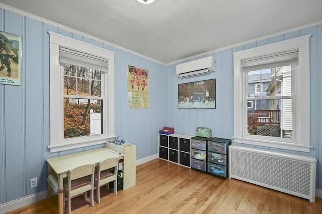 interior space with a wall mounted air conditioner, radiator heating unit, crown molding, light wood finished floors, and baseboards