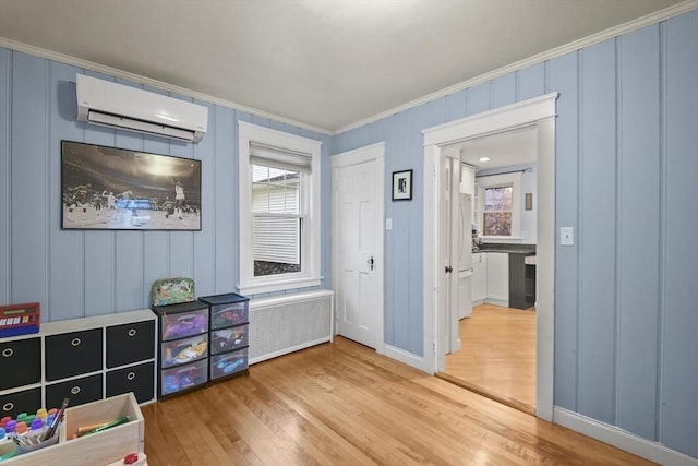 recreation room featuring ornamental molding, a wall mounted air conditioner, radiator heating unit, and wood finished floors