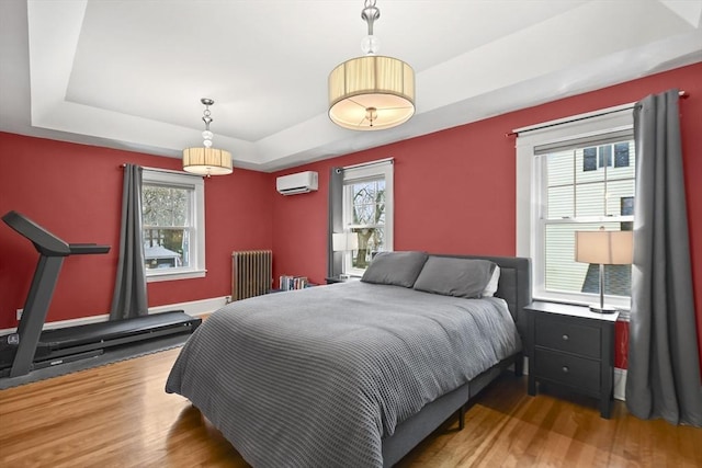 bedroom with a tray ceiling, wood finished floors, radiator heating unit, and a wall unit AC