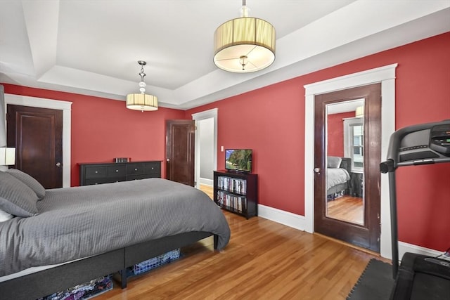 bedroom with a tray ceiling, baseboards, and wood finished floors