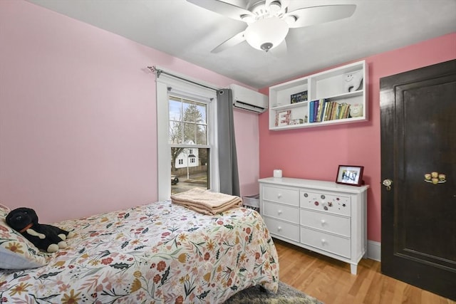 bedroom with a wall unit AC, light wood-style flooring, and a ceiling fan