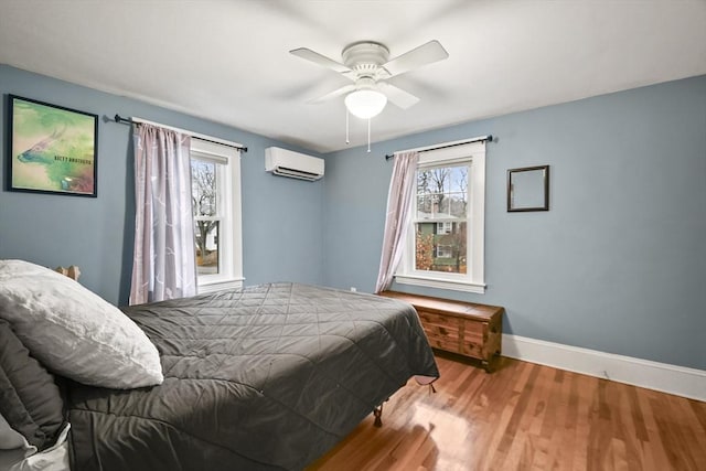 bedroom featuring a ceiling fan, a wall unit AC, wood finished floors, and baseboards