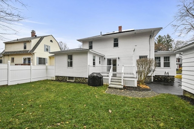 rear view of property with a deck, a yard, fence, and a chimney