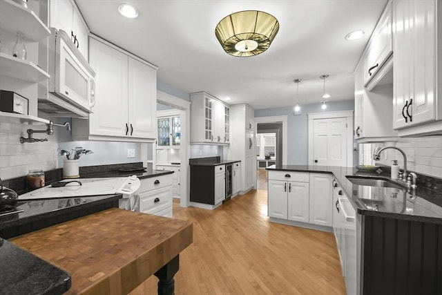 kitchen featuring a sink, dark stone countertops, white cabinetry, light wood-style floors, and glass insert cabinets