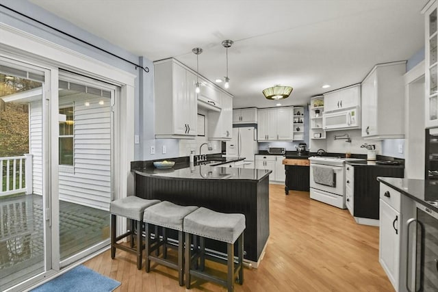 kitchen featuring dark countertops, light wood finished floors, a peninsula, white appliances, and open shelves