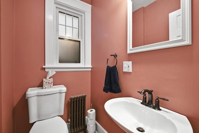 half bathroom featuring toilet, radiator heating unit, and a sink