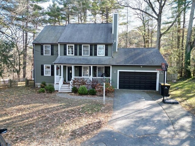 colonial inspired home with fence, an attached garage, a porch, a chimney, and driveway