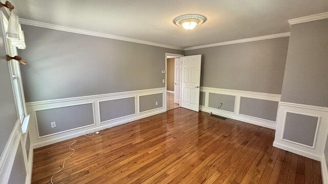 spare room with wood-type flooring, crown molding, visible vents, and wainscoting
