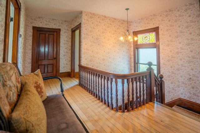 hall with wood-type flooring, a chandelier, wallpapered walls, an upstairs landing, and baseboards