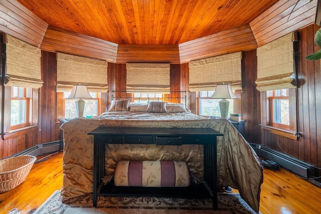 bedroom with wooden walls, baseboard heating, and hardwood / wood-style flooring