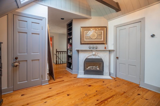 unfurnished living room with built in features, lofted ceiling, wood finished floors, baseboards, and a premium fireplace